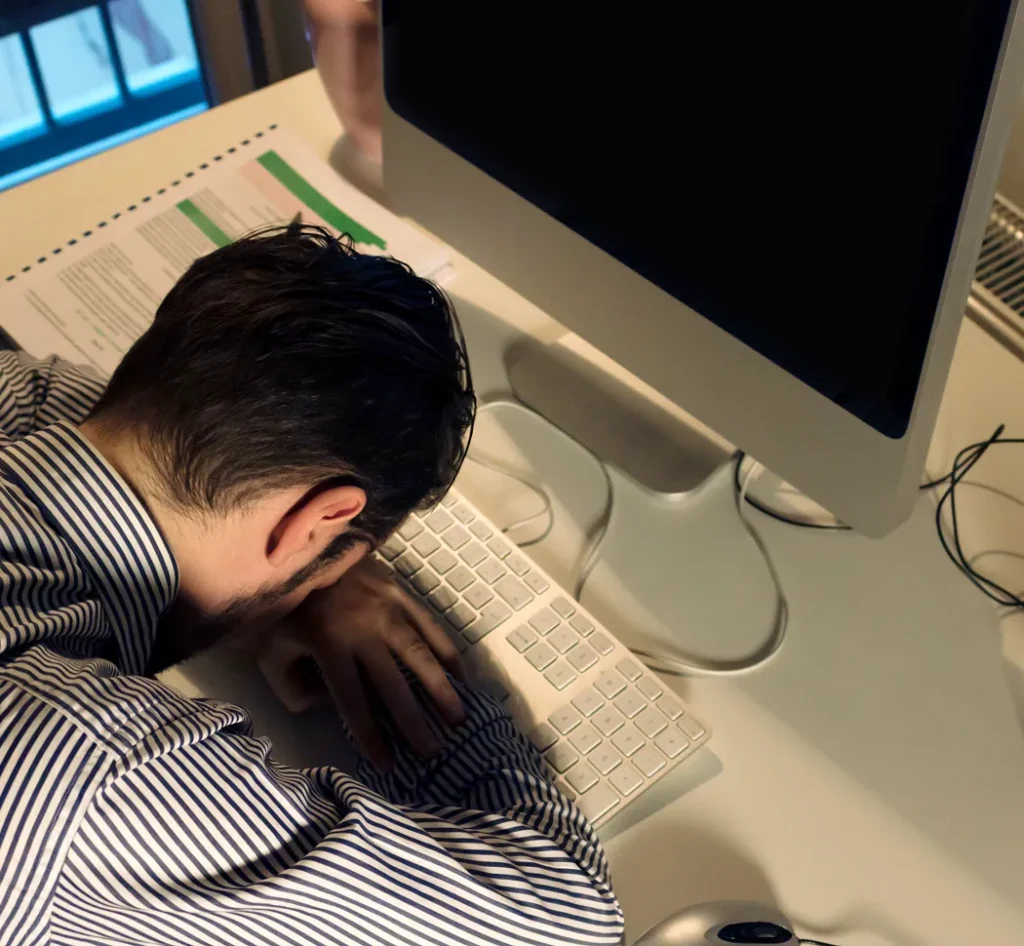 Gevolg van lage werknemerstevredenheid: medewerker met het hoofd op het toetsenbord zittend aan een bureau, ogenschijnlijk teneergeslagen of uitgeput.